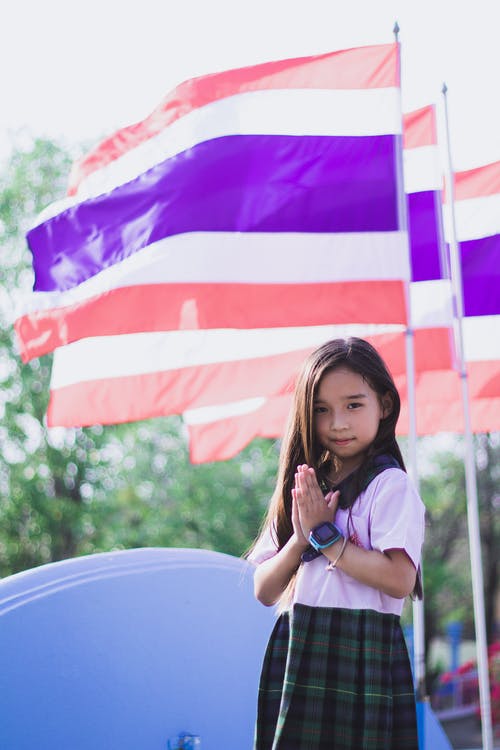 little girl wearing her school uniform standing next to a flag pole